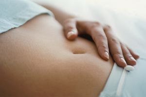 手放在女性腹部，由于过度排卵而感到浮肿和敏感＂width=