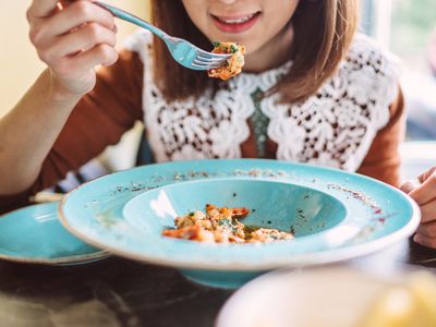 Young pretty Asian woman enjoying freshly served seafood pasta for lunch in a restaurant.