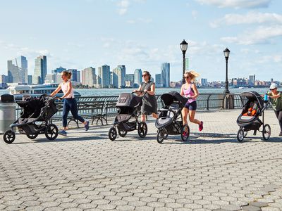 Four women running with jogging strollers with the New York City skyline in the background