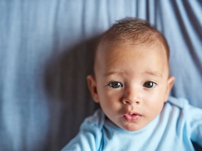 Baby wearing blue onesie on a blue sheet staring at the camera