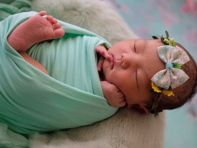 Baby swaddled in green blanket with a bow and flower headband