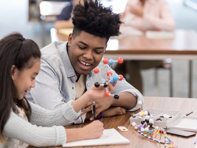 Girl draws molecule while teen helps
