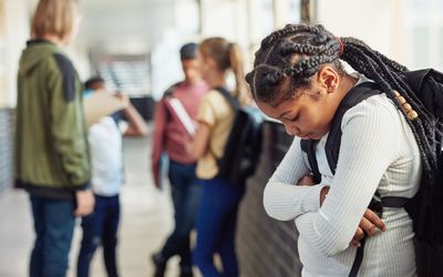 在学校的走廊里，一个小女孩被排除在同龄人之外，看起来很悲伤