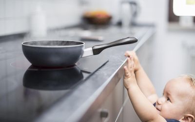 小男孩(1 y)试图够到炉子上的平底锅