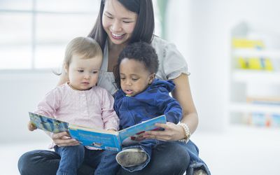 a babysitter holding a book and reading to two small children