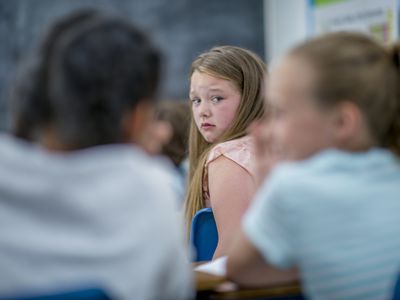 Two mean girls whispering about another girl in class.