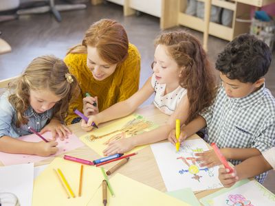 Young children draw with a teacher in a classroom.