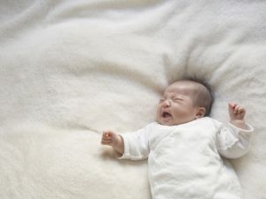 亚洲婴儿在白色毯子上哭泣。