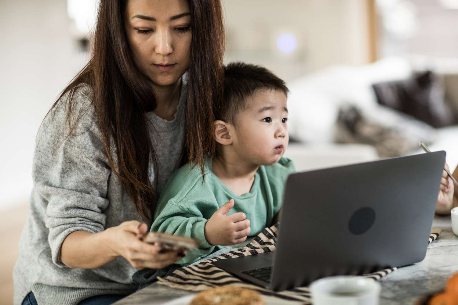 mom looks at her cellphone while baby sits on her lap