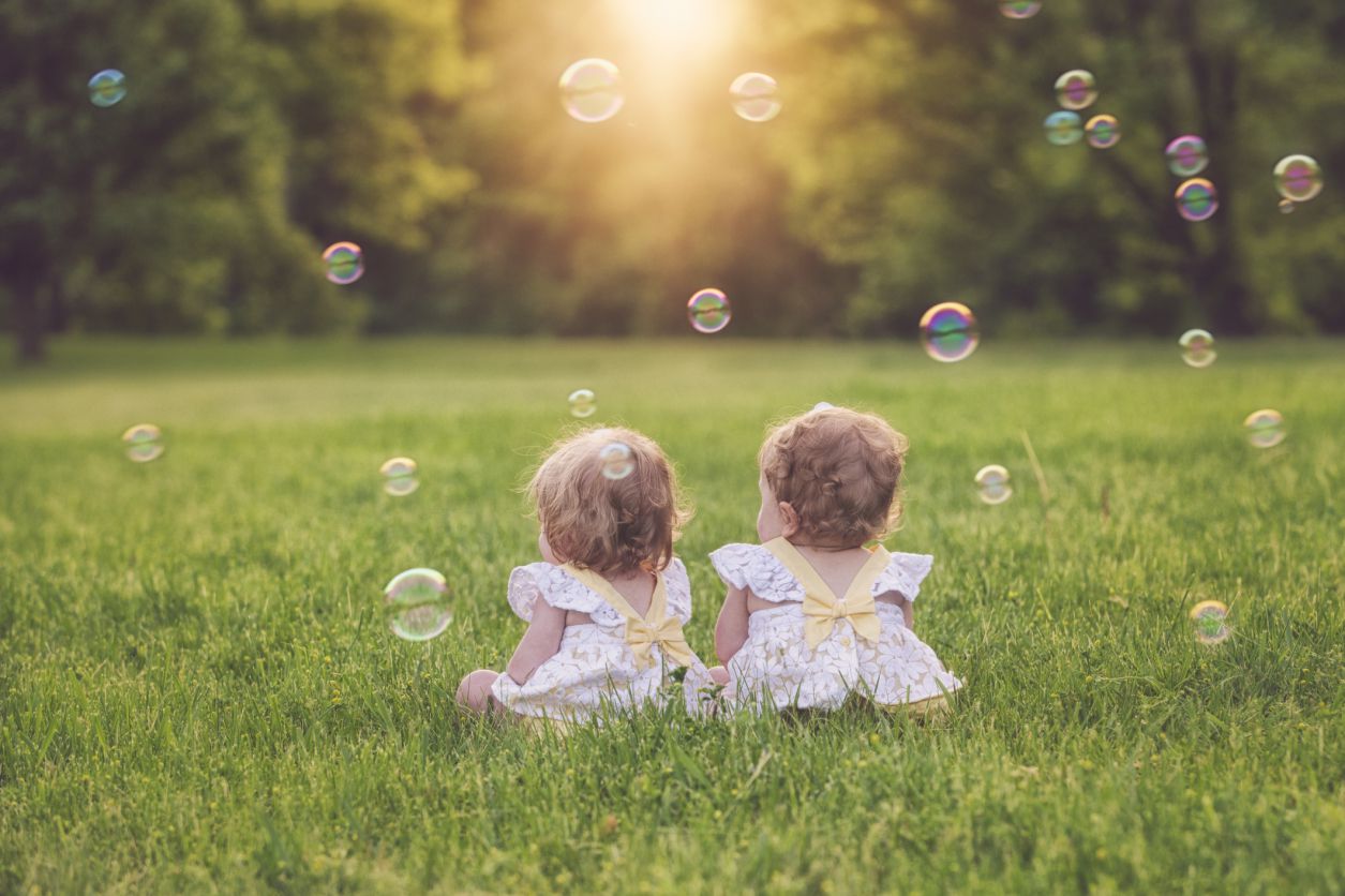 一对双胞胎女婴坐在草地上，带着泡泡