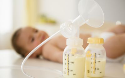 吸奶器防护罩上装有母乳的塑料瓶和背景中的婴儿