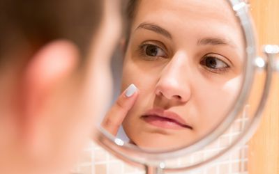 Woman looking into a close-up mirror, examining her skin.
