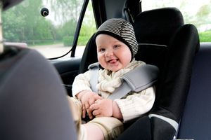 Baby wearing hat and sweater smiling in car seat.