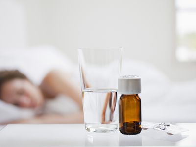 Close up of pill bottle with sick woman in background