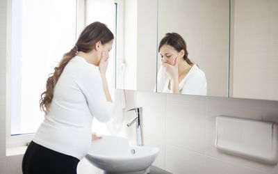 A pregnant woman looking nauseous standing at the bathroom sink