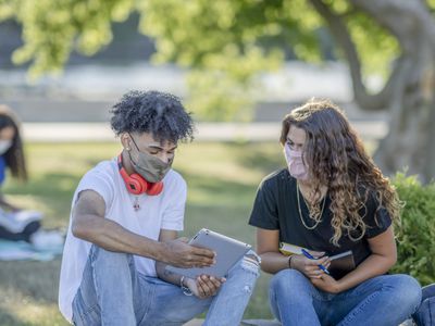 Two teens are sitting outside looking at an iPad