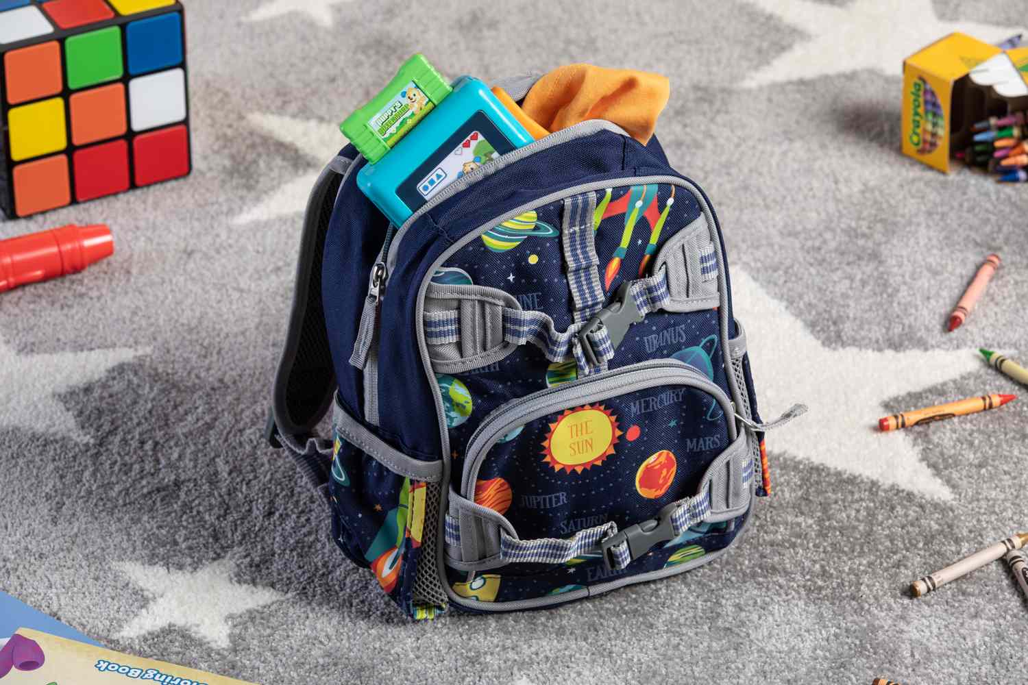 Pottery Barn Kids Mini Glow-in-the-Dark Mackenzie Backpack displayed on carpet floor with crayons
