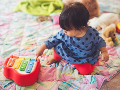 Toddler sitting on a blanket on the floor while playing with a toy piano