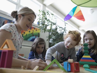 Preschool teacher and girl students playing with building blocks in classroom