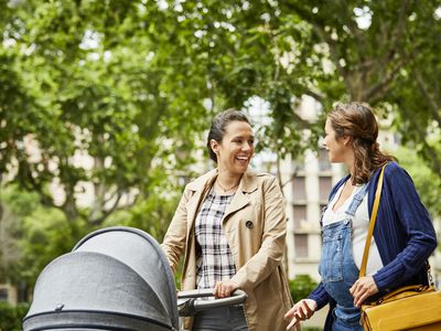 Two pregnant women talking, one of whom is pushing a stroller.