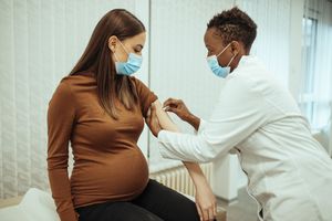 Pregnant woman prepares to receive vaccine by having her arm sanitized.