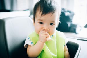 可爱的婴儿吃婴儿手指饼干在高椅子上存货照片