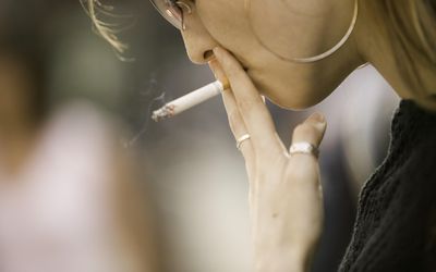 戴墨镜的年轻女子，在户外抽烟，特写