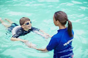 Young boy learning to swim in pool with teacher