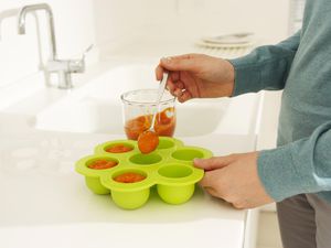 一个人用勺子舀着盛在托盘里准备冷冻的婴儿食品泥