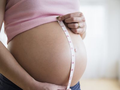 Mid section of pregnant woman measuring her belly